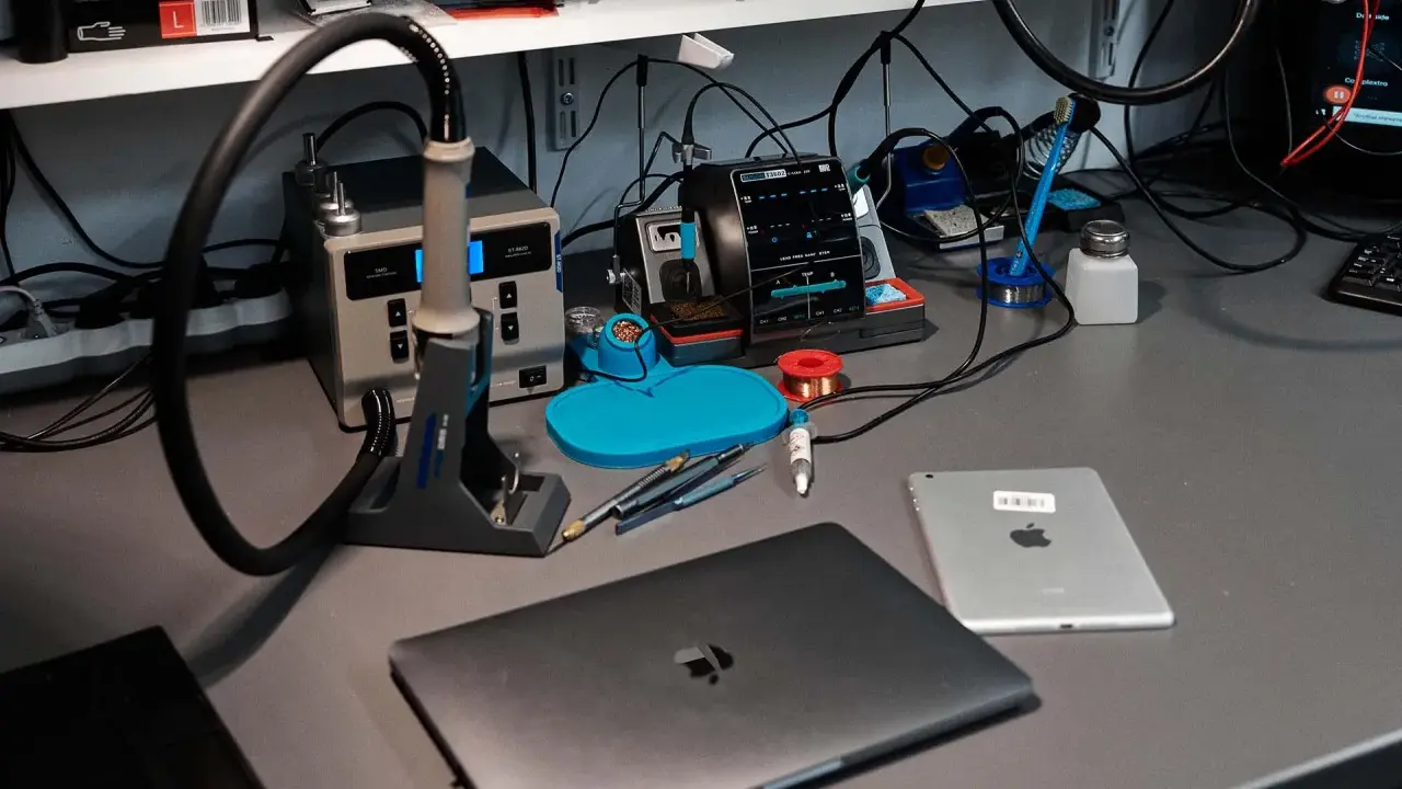Na biurku serwisowym leży zamknięty laptop, obok tablet. W tle widać stację lutowniczą i narzędzia.