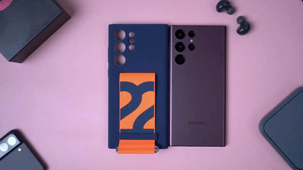 Granatowe etui na Samsung S22 z pomarańczowym paskiem, obok telefonu i słuchawek.