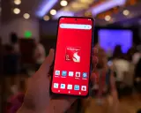Dłoń trzyma smartfon z czerwonym tłem i ikoną Snapdragon 8 Elite. Widoczne ikony benchmarków, sugerujące testowanie wydajności procesora.