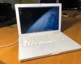 Biały, pierwszy MacBook z widokiem Ziemi na ekranie, stoi na drewnianym stole.