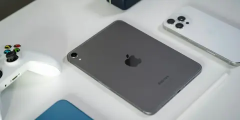 Szary iPad mini, biały kontroler do gier, biały iPhone i rysik na białym tle.