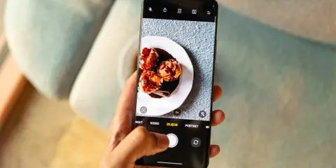 Dłoń trzyma telefon, na ekranie którego aparat robi zdjęcie pysznych ptysiów polanych czekoladą.