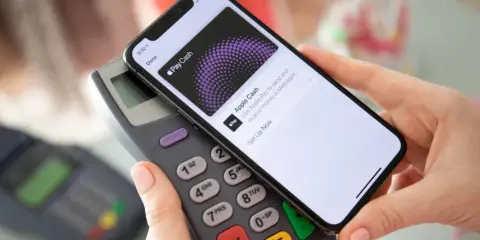 Dłoń zbliża telefon do terminala płatniczego, pokazując ekran Apple Pay. Tak łatwo można płacić telefonem.