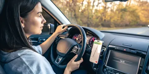 Kobieta prowadzi auto, a telefon z nawigacją zamontowany jest na desce rozdzielczej. Idealne miejsce, gdzie zamontować uchwyt na telefon w samochodzie.