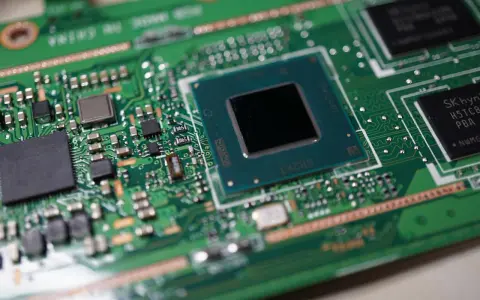 Zbliżenie na zieloną płytę główną z widocznymi częściami laptopa: procesorem, układami pamięci i innymi komponentami elektronicznymi.