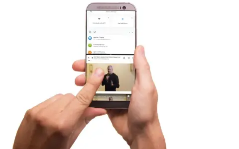 Dwie ręce trzymają telefon, na którym widać, jak podzielić ekran na 2. Górna część pokazuje ustawienia, dolna odtwarza wideo.