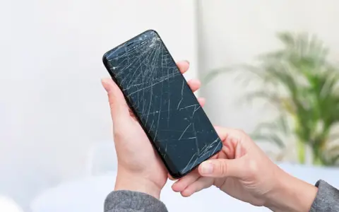 Dłoń trzyma pęknięty telefon, czekając na wymianę ekranu.