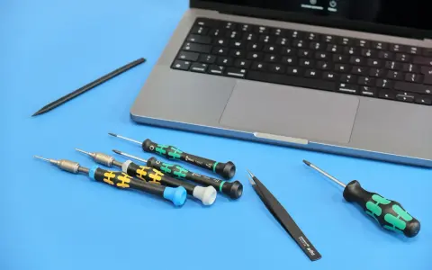 Narzędzia do naprawy iPhone'a: precyzyjne śrubokręty i pęseta obok laptopa. Przygotowanie do serwisu.