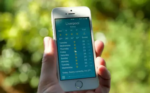 Dłoń trzyma smartfon z wyświetloną prognozą pogody dla Liverpoolu. To najlepsza aplikacja pogodowa, pokazująca słoneczną pogodę i temperatury na najbliższe dni.