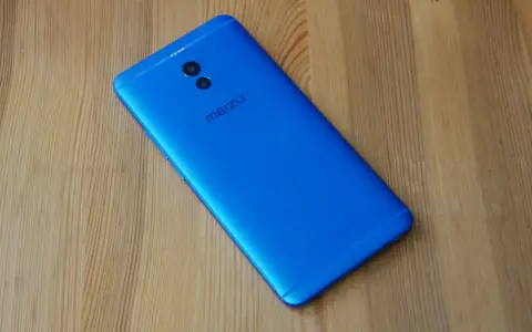 Niebieski smartfon Meizu M6 Note z podwójnym aparatem z tyłu leży na drewnianym blacie.