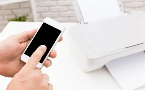 Instrukcja: jak połączyć telefon z drukarką. Smartfon w dłoni, obok drukarka z papierem.