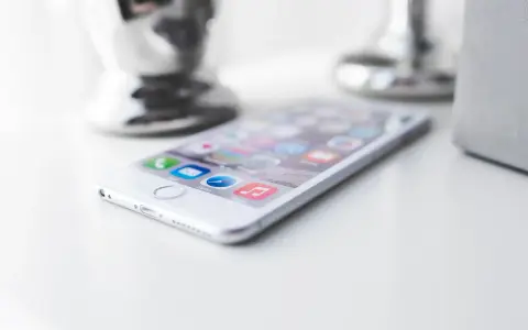 Biały iPhone leży na białym blacie, gotowy do pracy. W tle widać błyszczące i matowe elementy dekoracyjne.