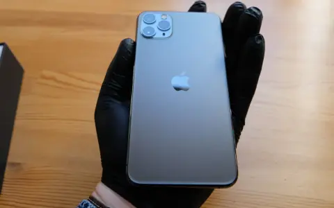 Ręka w czarnej rękawiczce trzyma elegancki iPhone 11 czarny. Obok leży czarne pudełko.