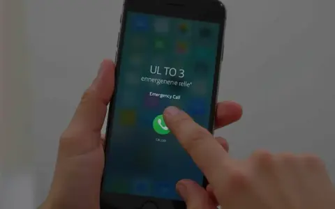 Dłoń naciska przycisk "Emergency Call" na ekranie telefonu, pokazując, jak odblokować telefon przez połączenie alarmowe.
