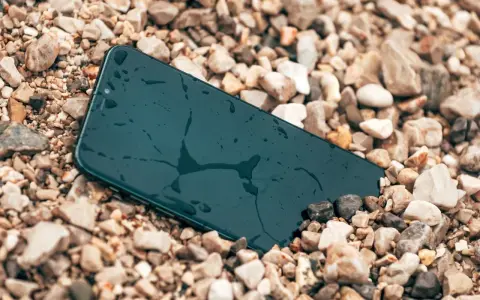 Smartfon leży na kamieniach, mokry, ale wytrzymały zgodnie ze **standardem militarnym MIL-STD-810H**.