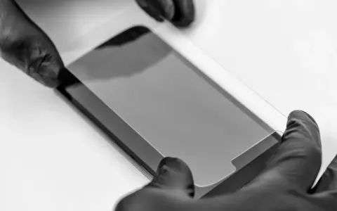 Ręce w czarnych rękawiczkach precyzyjnie nakładają szkło prywatyzujące na ekran smartfona, chroniąc prywatność.