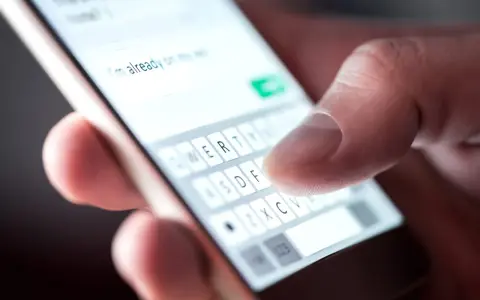 Palec pisze na klawiaturze telefonu, tworząc wiadomość. Widać fragment tekstu "I'm already on my way" i klawisze z literami. To klasyczny przykład polskie znaki w sms.