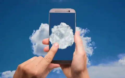 Dłonie trzymają telefon, na którego ekranie widać chmurę. To symbol tego, gdzie jest chmura w telefonie - w chmurze danych.