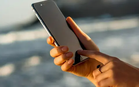Dłoń trzyma iPhone 13, który nie chce się włączyć. Palec wskazujący próbuje go ożywić.