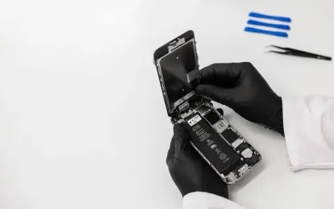 Ręce w czarnych rękawiczkach rozbierają iPhone'a, który wpadł do wody, ale działa. Widać baterię i wnętrze telefonu.