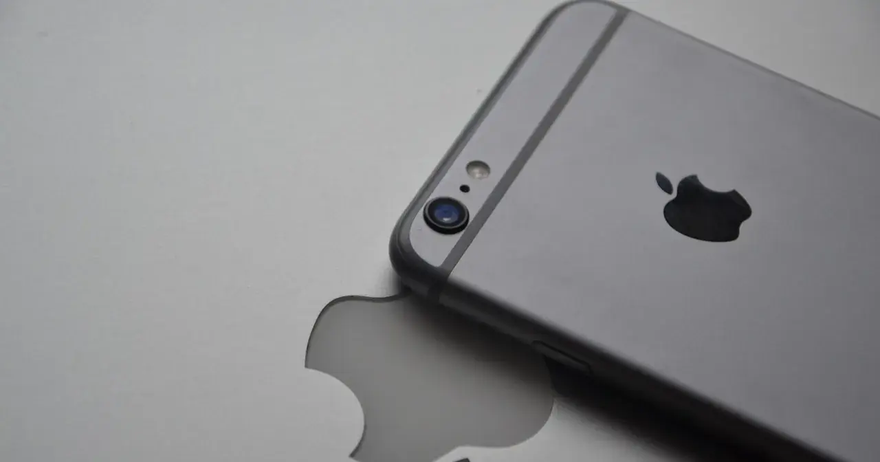 Srebrny iPhone leży na tle z wyciętym logo Apple, symbolizując spójność ekosystemu Apple.