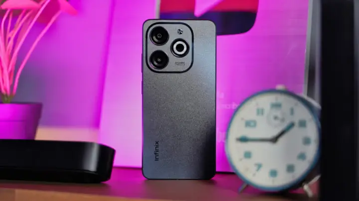 Szary smartfon Infinix z potrójnym aparatem na tle różowego światła. Czy to Infinix co to za firma?