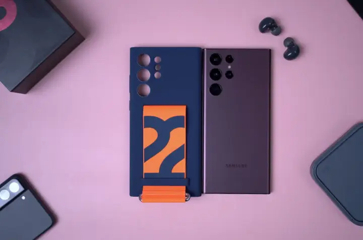 Granatowe etui na Samsung S22 z pomarańczowym paskiem, obok telefonu i słuchawek.